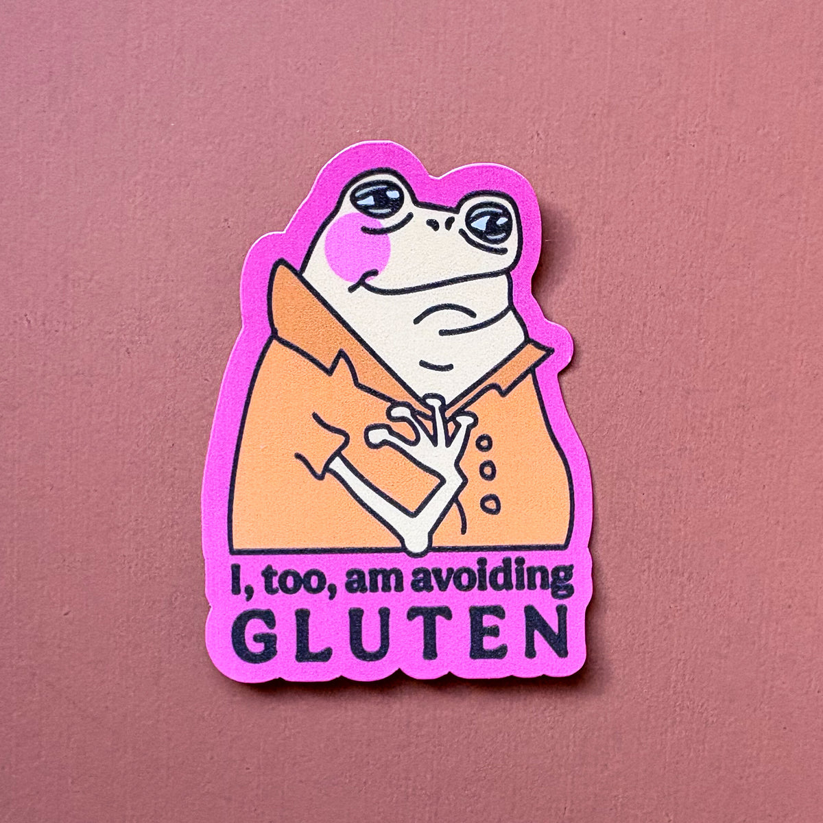 Frog sticker with orange shirt and pink border reading I, too, am avoiding GLUTEN, on a pink background