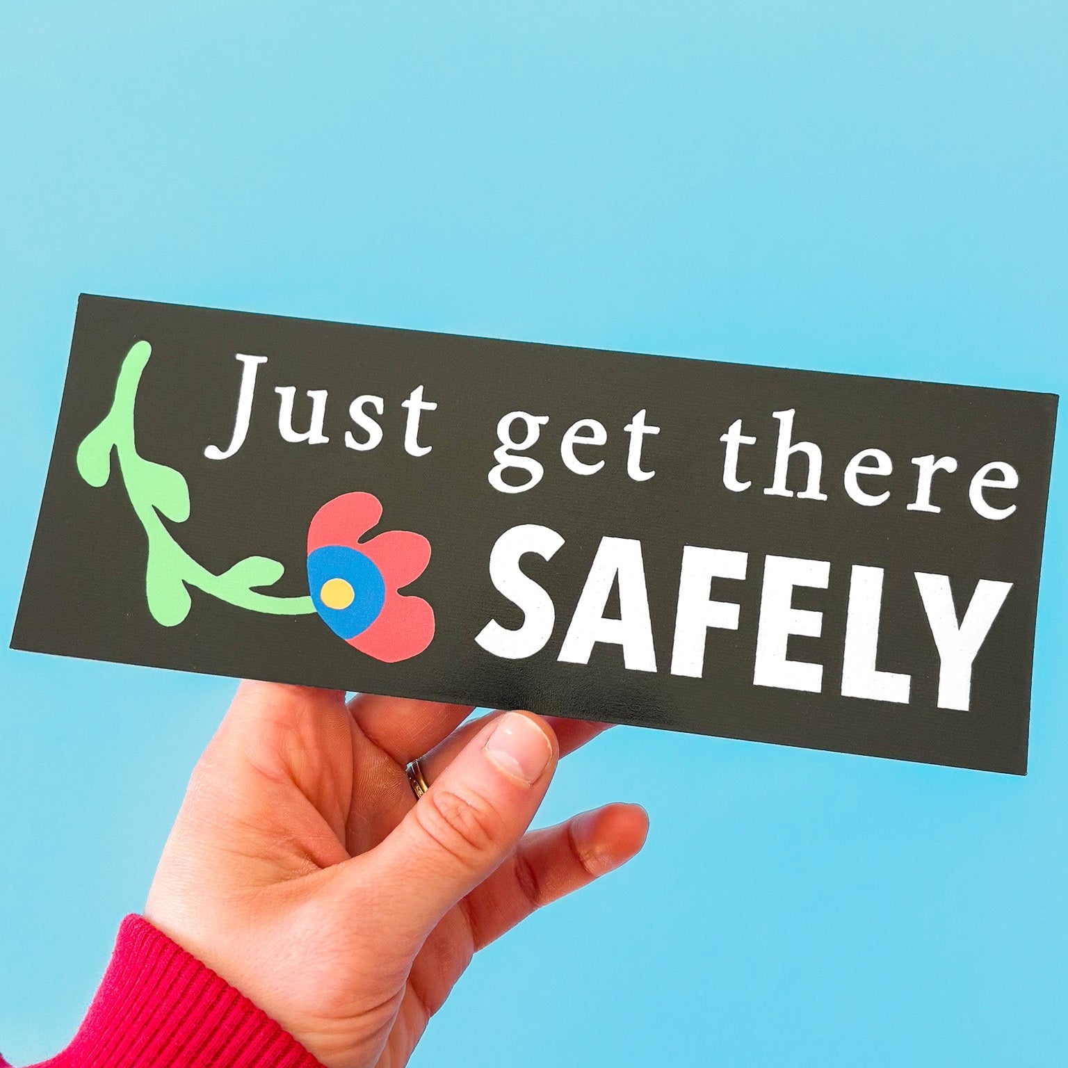 Hand holding a sign with 'Just get there SAFELY' text against a blue background