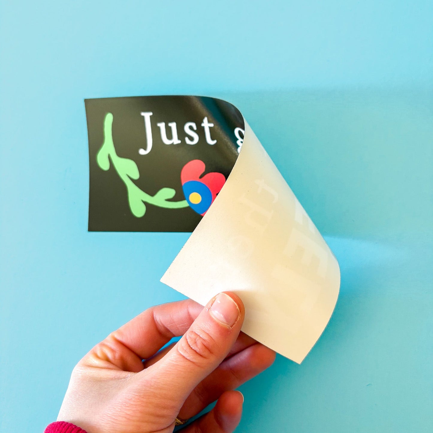 Hand holding a bumper sticker twisted to show white backing material on a blue surface.