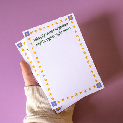 Hand holding two sheets of paper with decorative border and text on a purple background