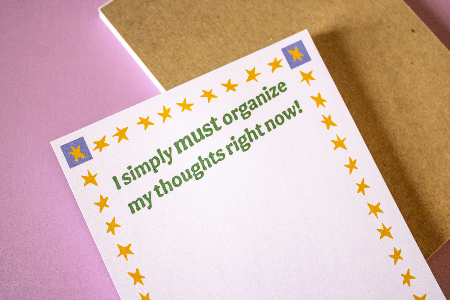 Notepad with text 'I simply must organize my thoughts right now!' on a pink and brown background