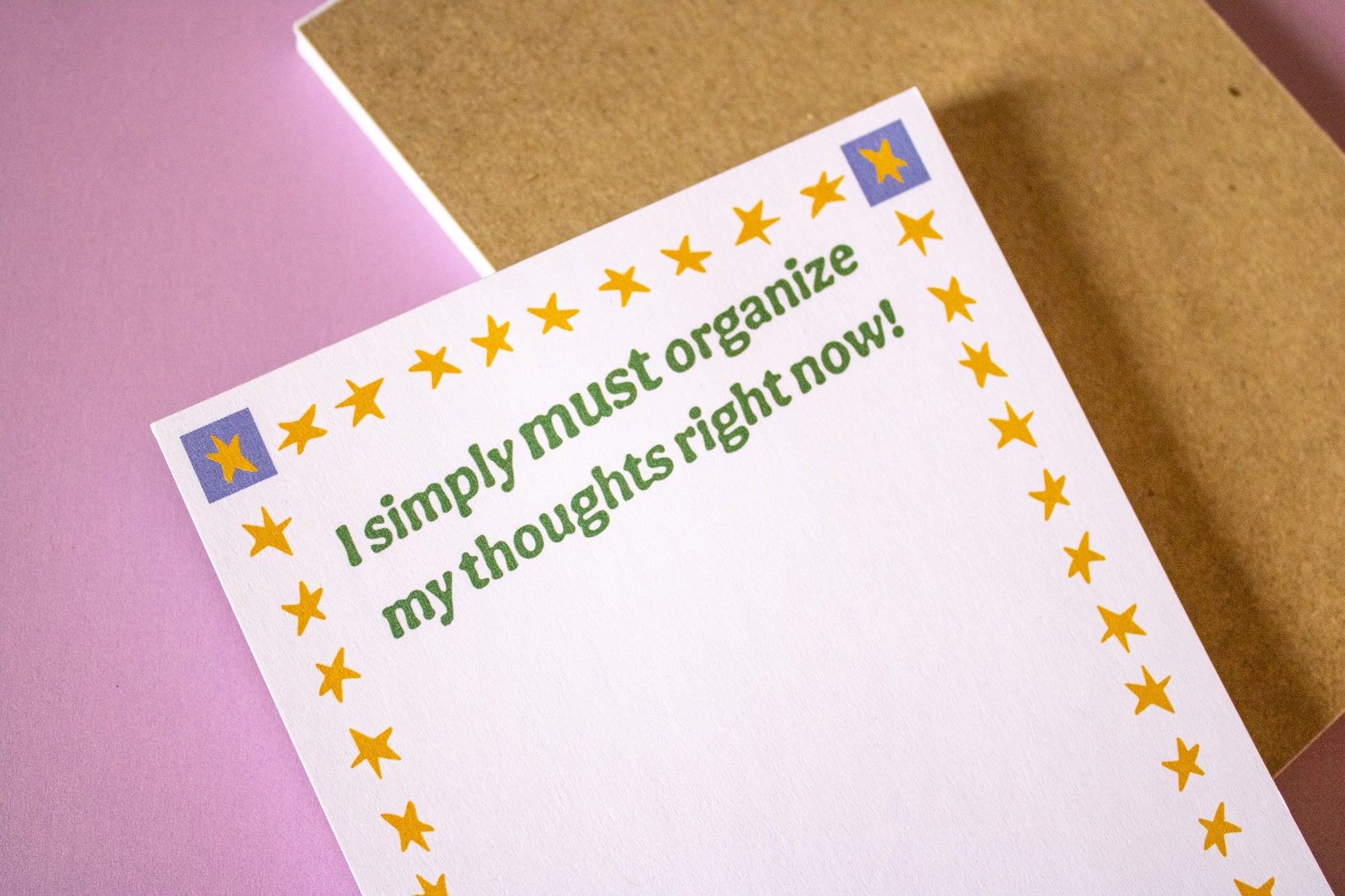 Notepad with text 'I simply must organize my thoughts right now!' on a pink and brown background
