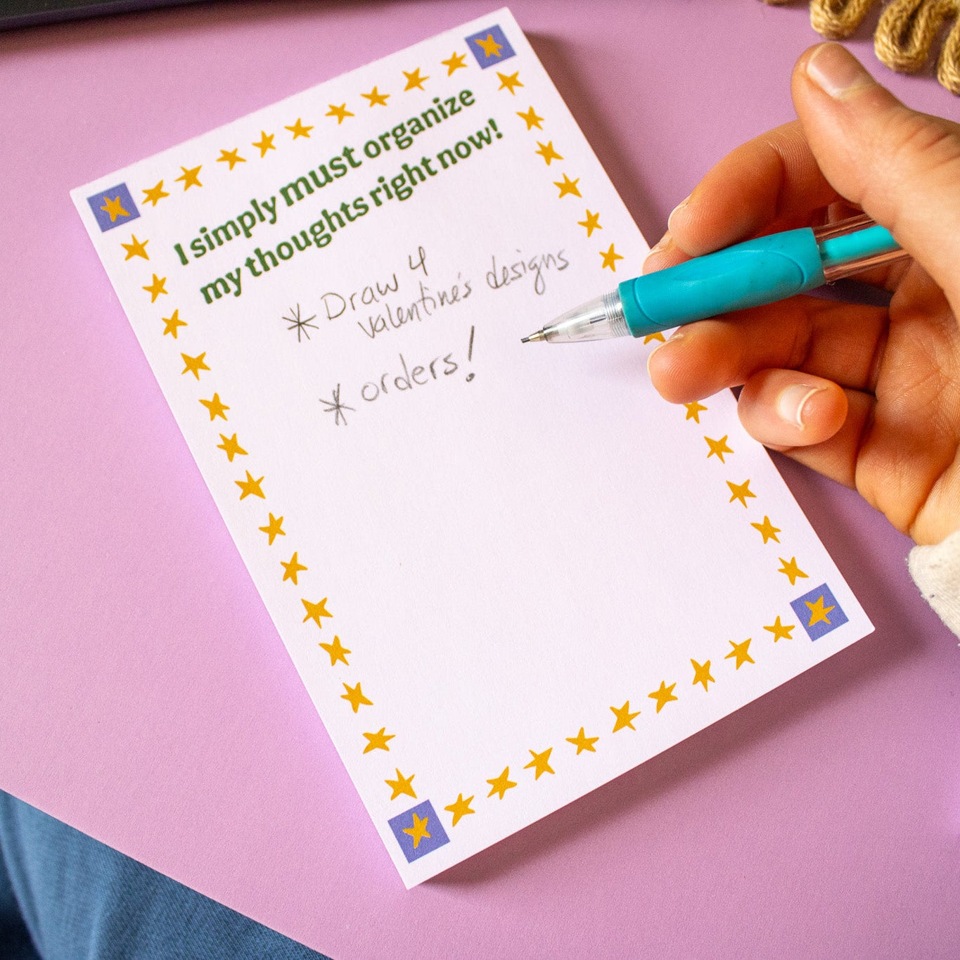 Hand holding a pen over a notepad with text on a pink surface