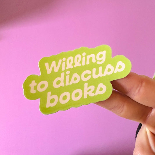 Green sticker with 'Willing to discuss books' text held against a pink background